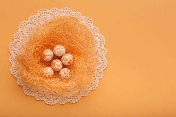 Nest with colored eggs, as a symbol of Easter on orange background with copy space for greeting text.