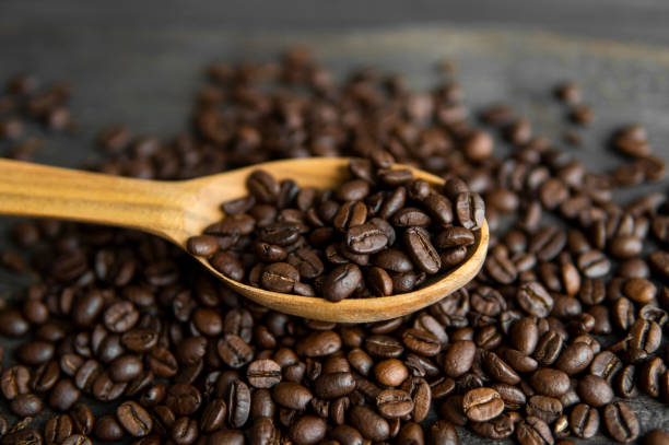 Fresh roasted arabica coffee beans in a wooden spoon and scattered coffee beans on a wooden table. stock photo