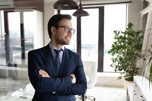 Smiling Caucasian businessman in formal suit glasses look in distance visualize think of future career success. Happy male CEO or boss make plans or decision in office. Business vision concept.