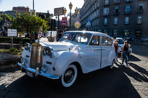 Naples, Italy - September 9, 2019: Old retro white Rolls Royce car decorated with wedding decorations on a street with people around in Naples, Italy