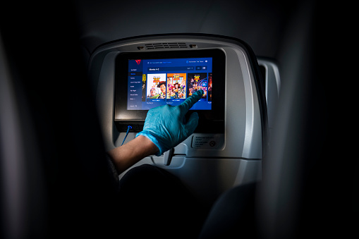 A passenger aboard a Delta Airlines flight from New York City's LaGuardia airport to Atlanta wears a latex glove while touching the inflight entertainment screen to select a movie to watch.(March 21, 2020)