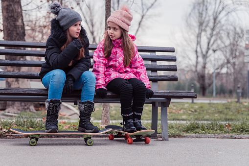 Serious young girls sitting on a bench and having skateboards under their feet