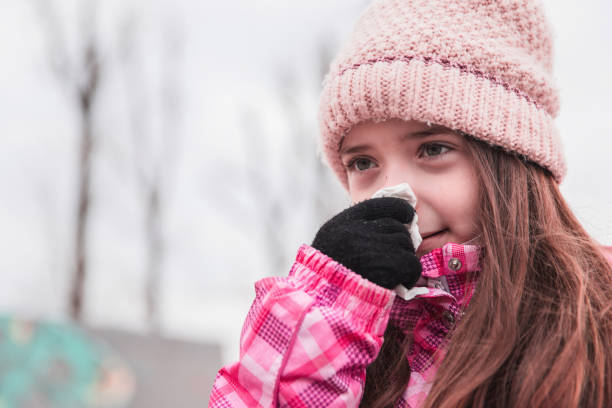 Girl wearing a hat and gloves wiping nose with a tissue