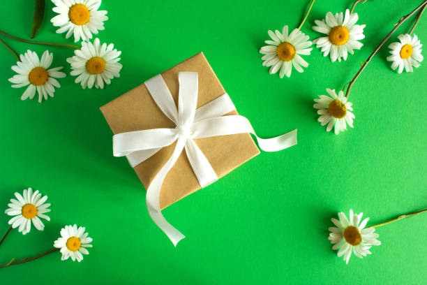 istock Gift box with white ribbon  and chamomile on the green background.Top view. 1307800501