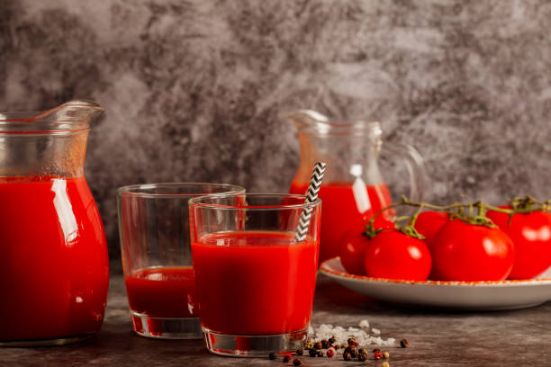 jus de tomate frais dans un verre avec le sel de tomates et le poivre sur un fond foncé. boisson végétale de tomate pour une alimentation saine sur un fond gris. vue du haut. - tomato juice drink celery juice photos et images de collection