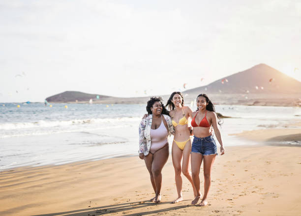 schöne latin frauen mit verschiedenen körpern und hautfarbe zu fuß am strand - millennial mädchen mit spaß zusammen in den sommerferien - beach body stock-fotos und bilder