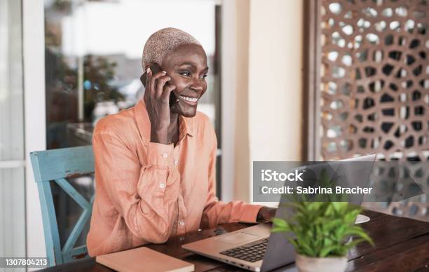 Mature Black Woman Working With Laptop Outdoor While Talking On Smartphone Call Stock Photo - Download Image Now