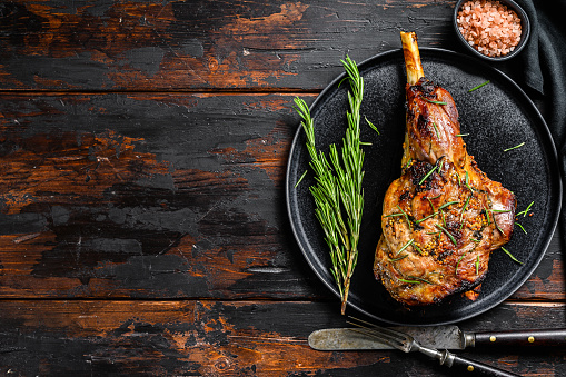 Baked lamb, sheep leg with rosemary.  Dark wooden background. Top view. Copy space.