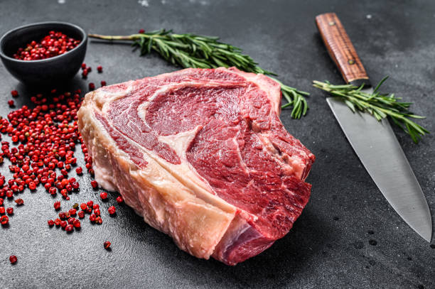 Raw cowboy steak or ribeye on the bone with herbs. Marble beef. Black background. Top view. Raw cowboy steak or ribeye on the bone with herbs. Marble beef. Black background. Top view marbled meat stock pictures, royalty-free photos & images