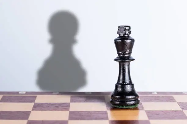 Black chess king with pawn shadow. Exaggeration of possibilities concept.