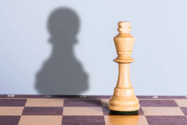 White chess king with pawn shadow. Exaggeration of possibilities concept.
