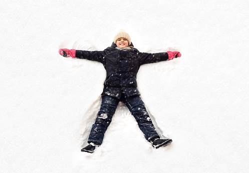 A little girl playing in the snow in winter. Happy child lying down makes a snow angel