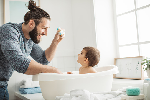 Young father bathing cute toddler baby in bathroom at home