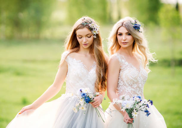 여름 들판에서 화창한 날에 야생 꽃다발과 흰색 웨딩 드레스를 입은 두 명의 아름다운 신부 들러리 - princess women beautiful 20s 뉴스 사진 이미지