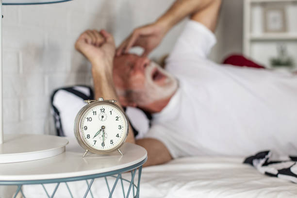 homme aîné se réveillant avec l’alarme - pillow wake up yawning sleeping photos et images de collection