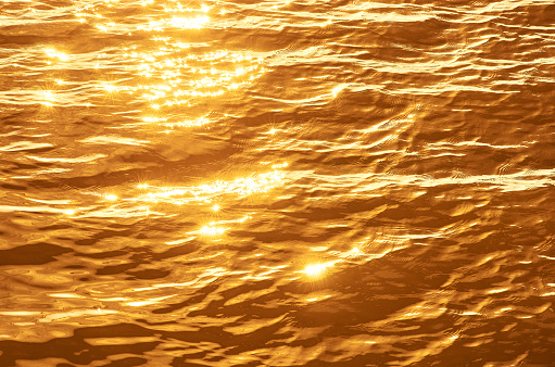 Shiny yellow-orange sunset light reflected in rippled water surface background