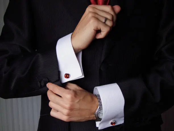 Hands adjusting cuffs of the shirt fastened with a pair of red glass cufflinks before a wedding