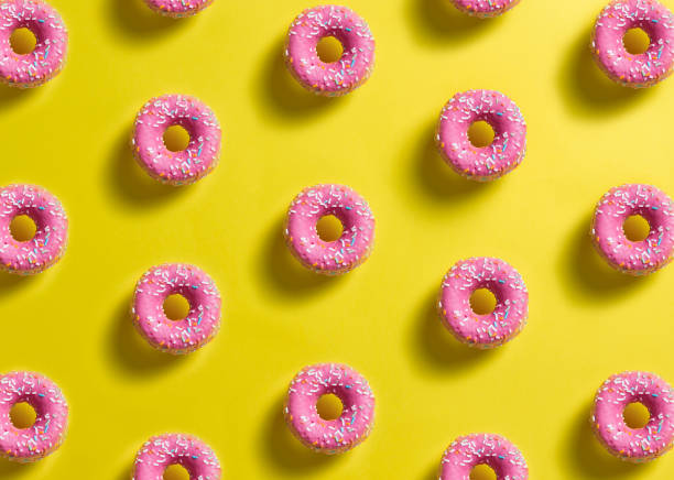 istock pattern of pink donuts decorated with colored confetti with shadow on lemon yellow background 1307829254