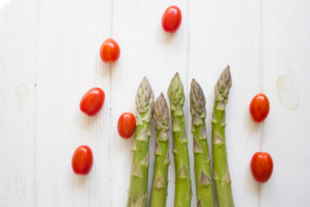 Green Asparagus and cherry tomatoes isolated on white wood. Top view