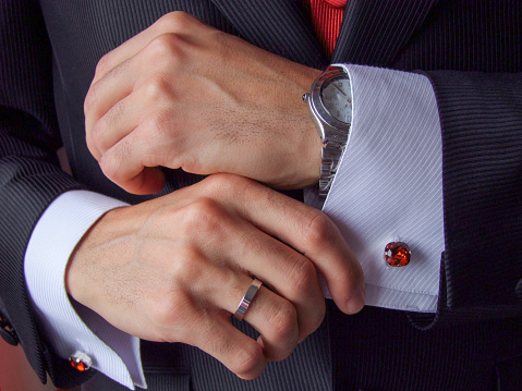 Manos masculinas de hombre blanco en primer plano sosteniendo puño de camisa blanca de ceremonia con gemelos rojos, anillo y reloj photo
