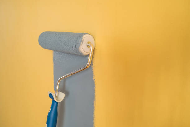 istock Paint Roller with Blue Paint on a Yellow Wall 1307833266