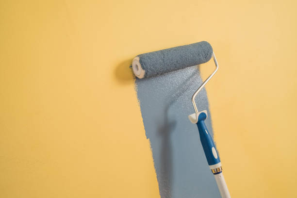 istock Paint Roller with Blue Paint on a Yellow Wall 1307833278