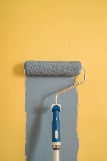 istock Paint Roller with Blue Paint on a Yellow Wall 1307833284
