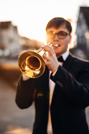 Trumpet Player in the City. Well-dressed young man in black suit with bow tie playing a trumpet in the city during sunset. Backlit from the sunset light. Small DOF, Selective Focus on Trumpet. Trumpet Player Millennial Generation Portrait.