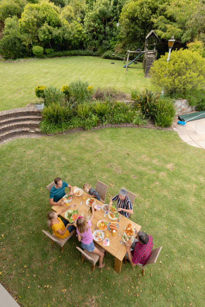 vue d’angle élevé de famille caucasienne de trois générations se reposant au repas de manger de table dans le jardin - high angle view photos et images de collection