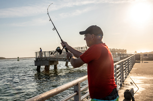 Senior man fishing on a pier by the sea in Florida during springtime.