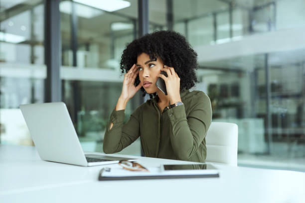 Another day, another spam caller Shot of a young businesswoman looking stressed while using a laptop and smartphone in a modern office information overload photos stock pictures, royalty-free photos & images