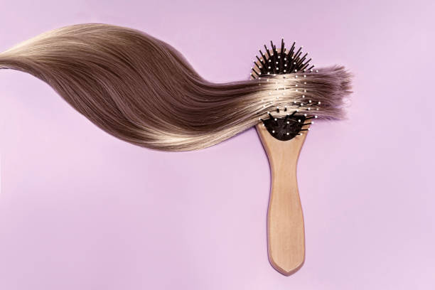 Strand of hair on a wooden comb. A smooth blonde strand of hair on a wooden comb. On a pink background, top view. hair strands stock pictures, royalty-free photos & images