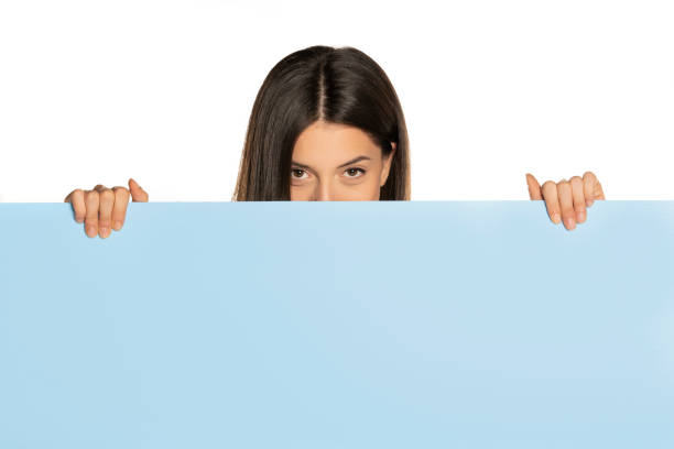 istock young beautiful woman peeking behind a blue empty board 1307843604