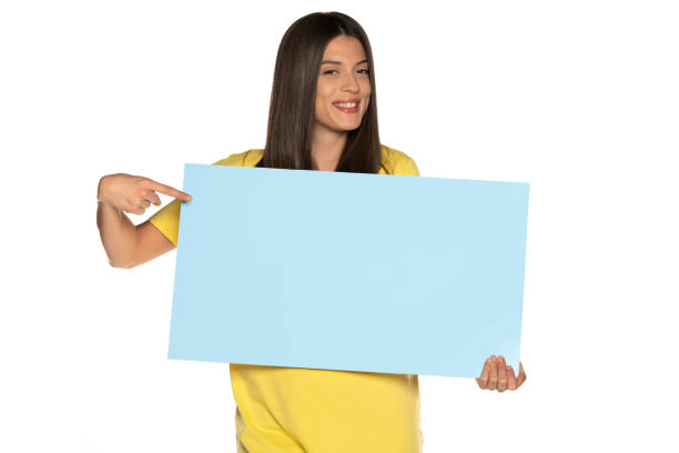 istock young beautiful happy woman holding and pointing on a blue empty board 1307843617