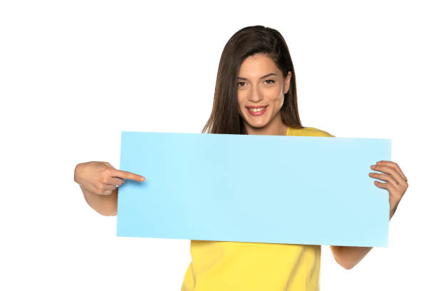 istock young beautiful happy woman holding and pointing on a blue empty board 1307843645