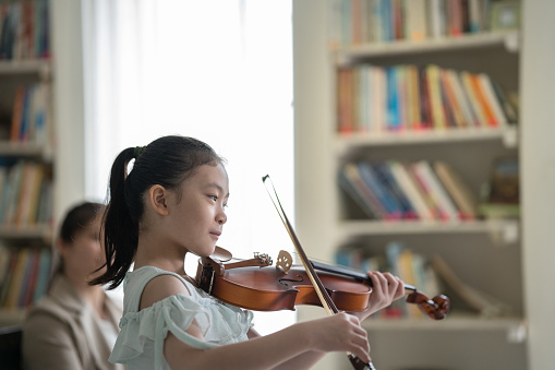 Young blonde girl plays violin on a white studio background.