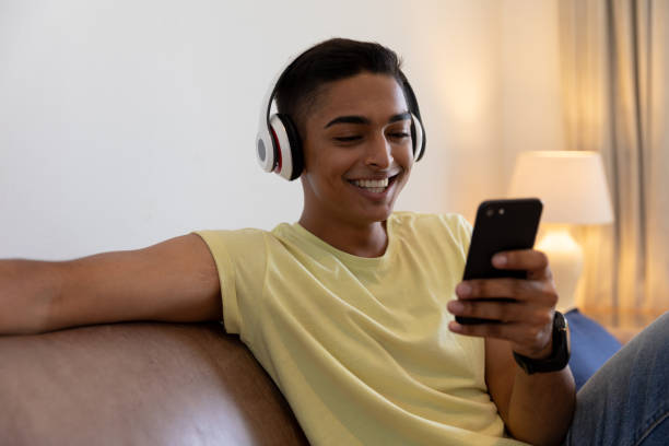 istock Mixed race man sitting on couch wearing headphones smiling and using smartphone 1307847026