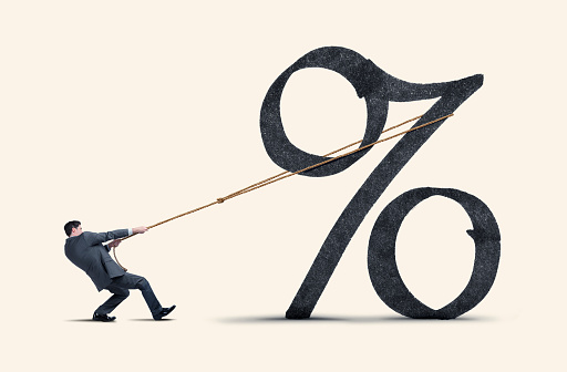 A man attempts to lift a large interest rate symbol with a rope.