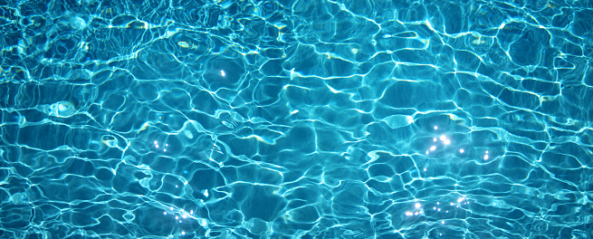 Blue water in swimming pool with sun reflections, natural background