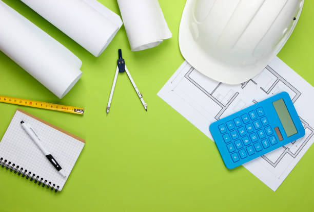istock Engineering construction safety helmet, blueprint rolls, project plan and calculator on green background. Calculation of the cost building a house. Top view. Flat lay 1307857805
