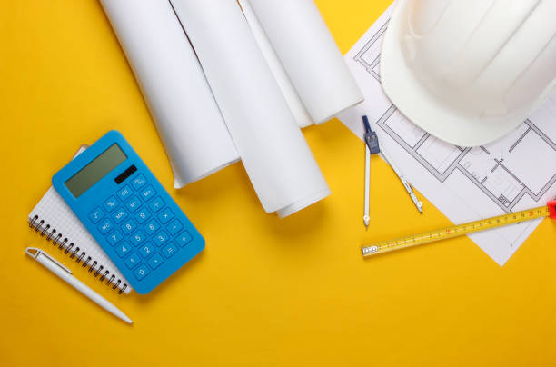 istock Engineering construction safety helmet, blueprint rolls, project plan and calculator on yellow background. Calculation of the cost building a house. Top view. Flat lay 1307857818