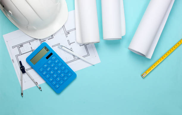 istock Engineering construction safety helmet, blueprint rolls, project plan and calculator on blue background. Calculation of the cost building a house. Top view. Flat lay 1307857858