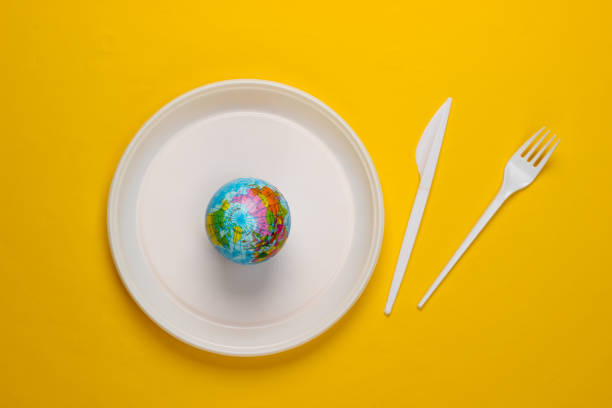 istock Eco concept. Plastic pollution. Globe in a plastic plate, fork and knife on yellow background. Top view 1307863424