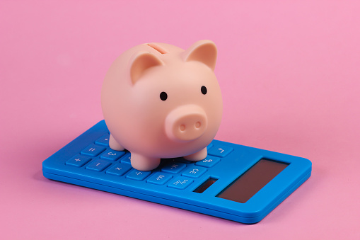 Piiggy bank with calculator close-up on a pink pastel background. Calculation of the family budget, saving. Minimalism