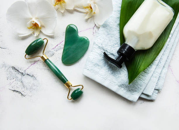 istock Face massage jade roller with cosmetic product on white marble background 1307865302