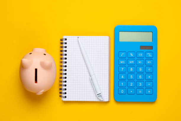 istock Piggy bank, notebook and calculator on yellow background. Minimalistic studio shot. Overhead view. Flat lay. 1307867301