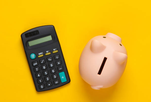 istock Piggy bank and calculator on yellow background. Minimalistic studio shot. Overhead view. Flat lay. 1307867430