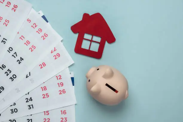 Piggy bank with a monthly calendar, house figure on blue background. Payment of rental housing or loans. Top view