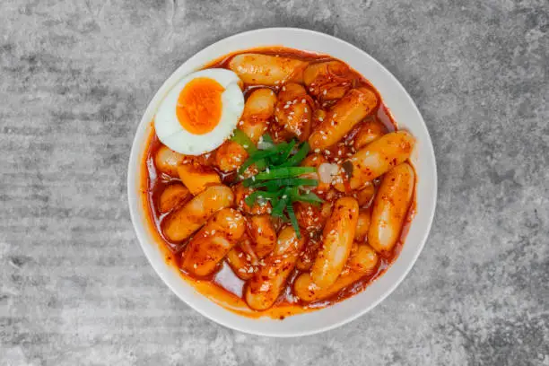 Top view Tteokbokki (Spicy Rice Cakes) with boiled eggs on the grey concrete table, Korean street food.