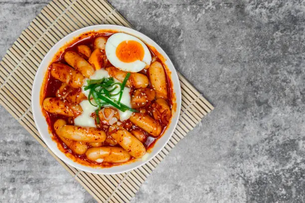 Top view Tteokbokki (Spicy Rice Cakes) with boiled eggs and cheese on the grey concrete table, Korean street food.